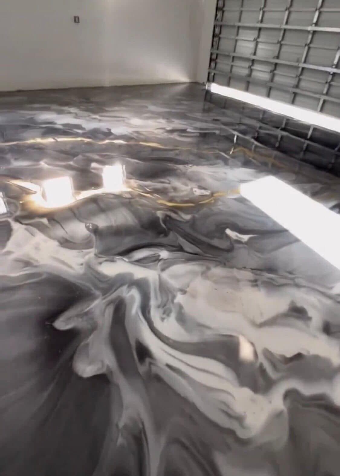 A glossy black-and-gold metallic epoxy garage floor swirling like poured marble under shop lights.